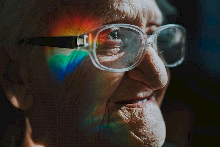 Older Man with glasses on, reflection of a rainbow on his face.