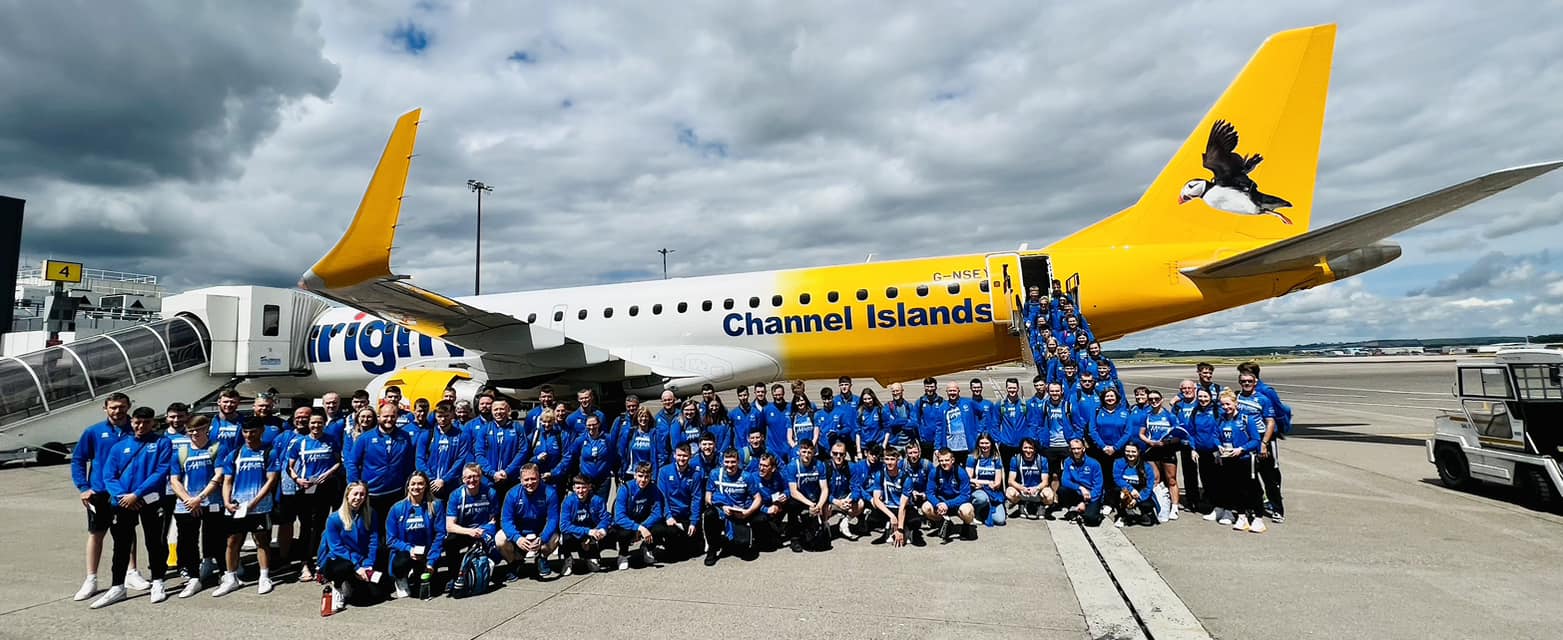 Members of "Team Shetland" dressed in blue tops and black trousers, lined up in front of a yellow and white aeroplane 