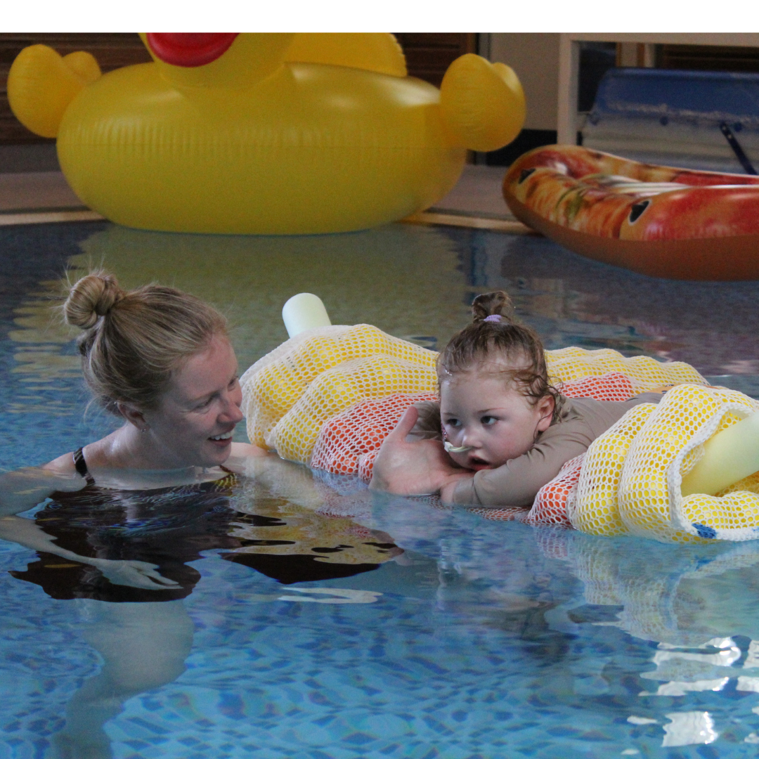 Young child lying on her belly on a float in a pool, looking relaxed. Mother in the pool to the left of the child looking happy.