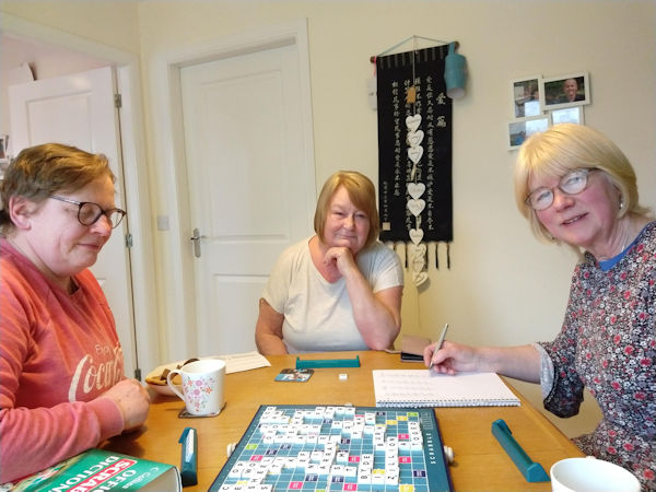 Three people sitting at a table playing the board game Scrabble.