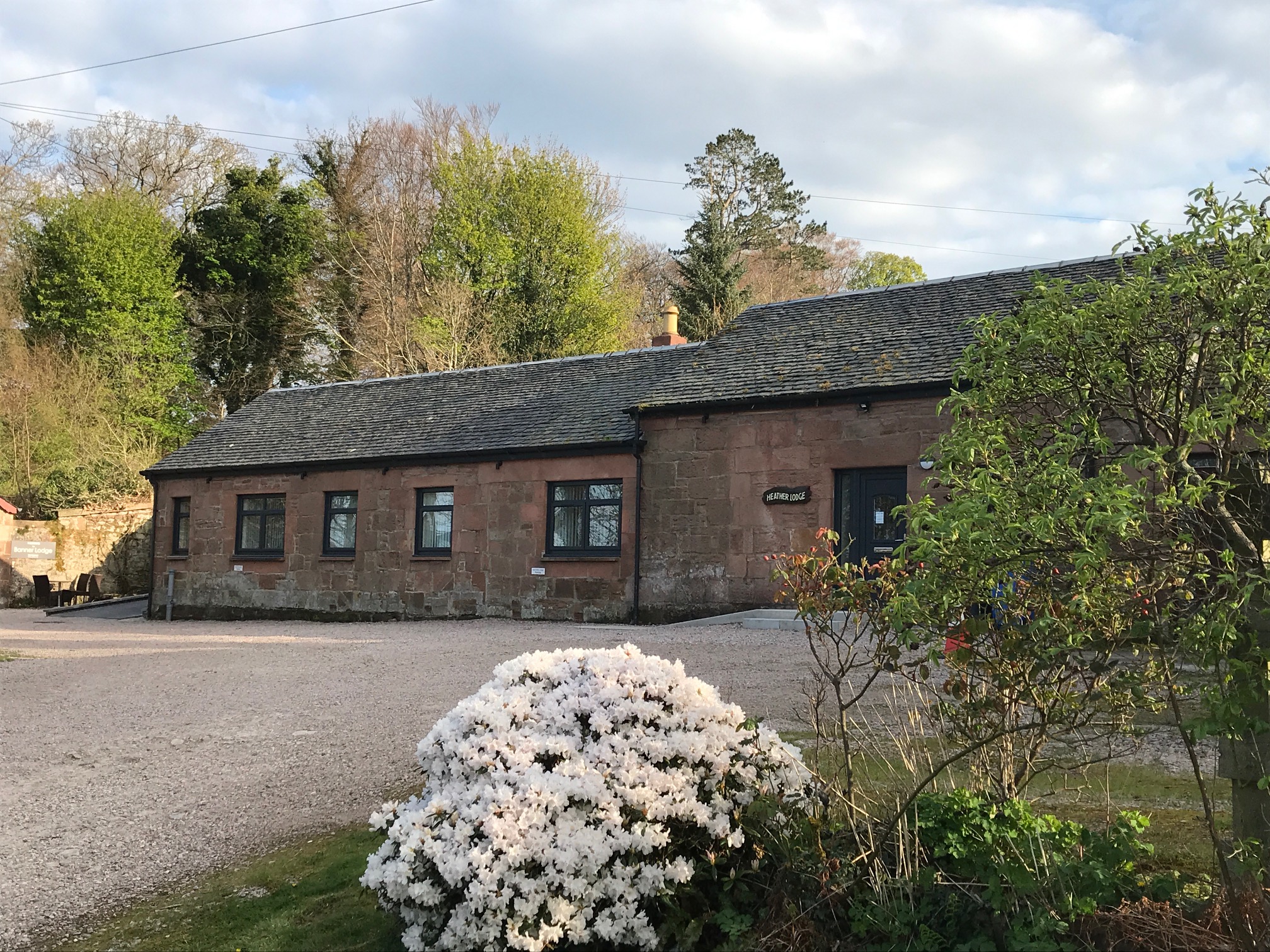 Large old stone building surrounded by large green trees, the sky is filled with white fluffy clouds.