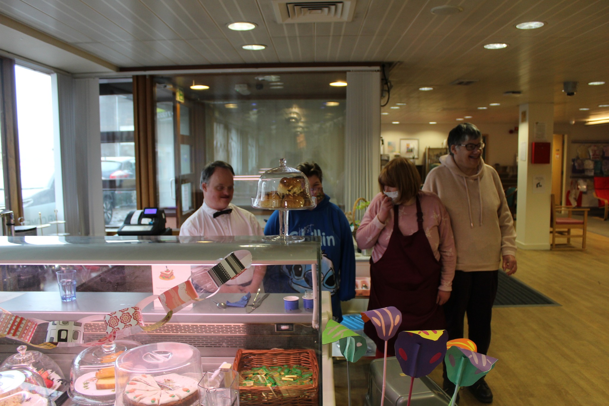 The Vintage Cafe is pictured with some volunteers smiling behind a cabinet full of cakes.