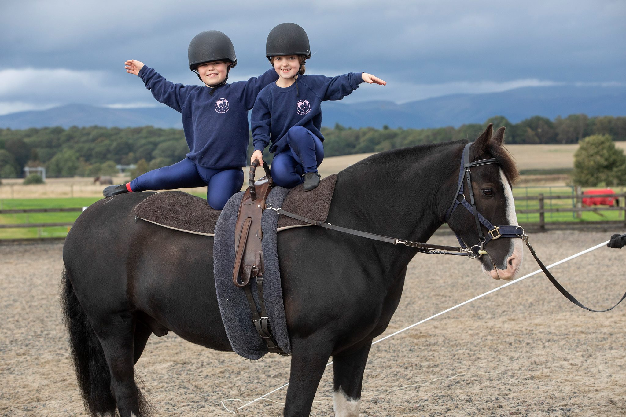 Two children sitting on top of a horse, they looking at the camera and waving.ving