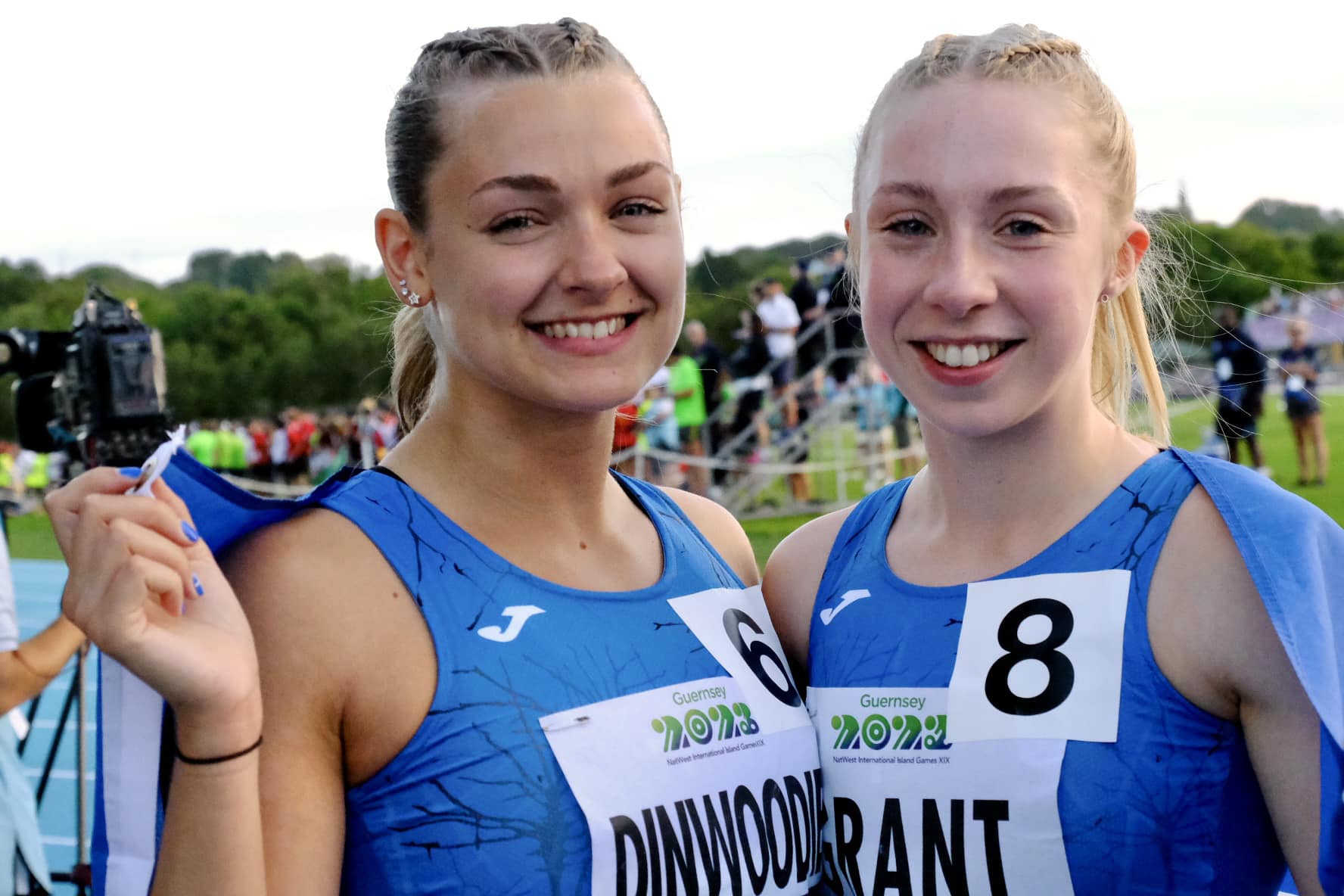 Two track athletes -  wearing blue tops, smiling at the camera.