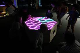 Image shows people around a wooden sculpture with interactive LED lights on top in a wavy pattern