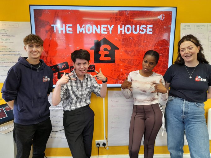 Two trainers and two young people smiling in front of The Money House logo