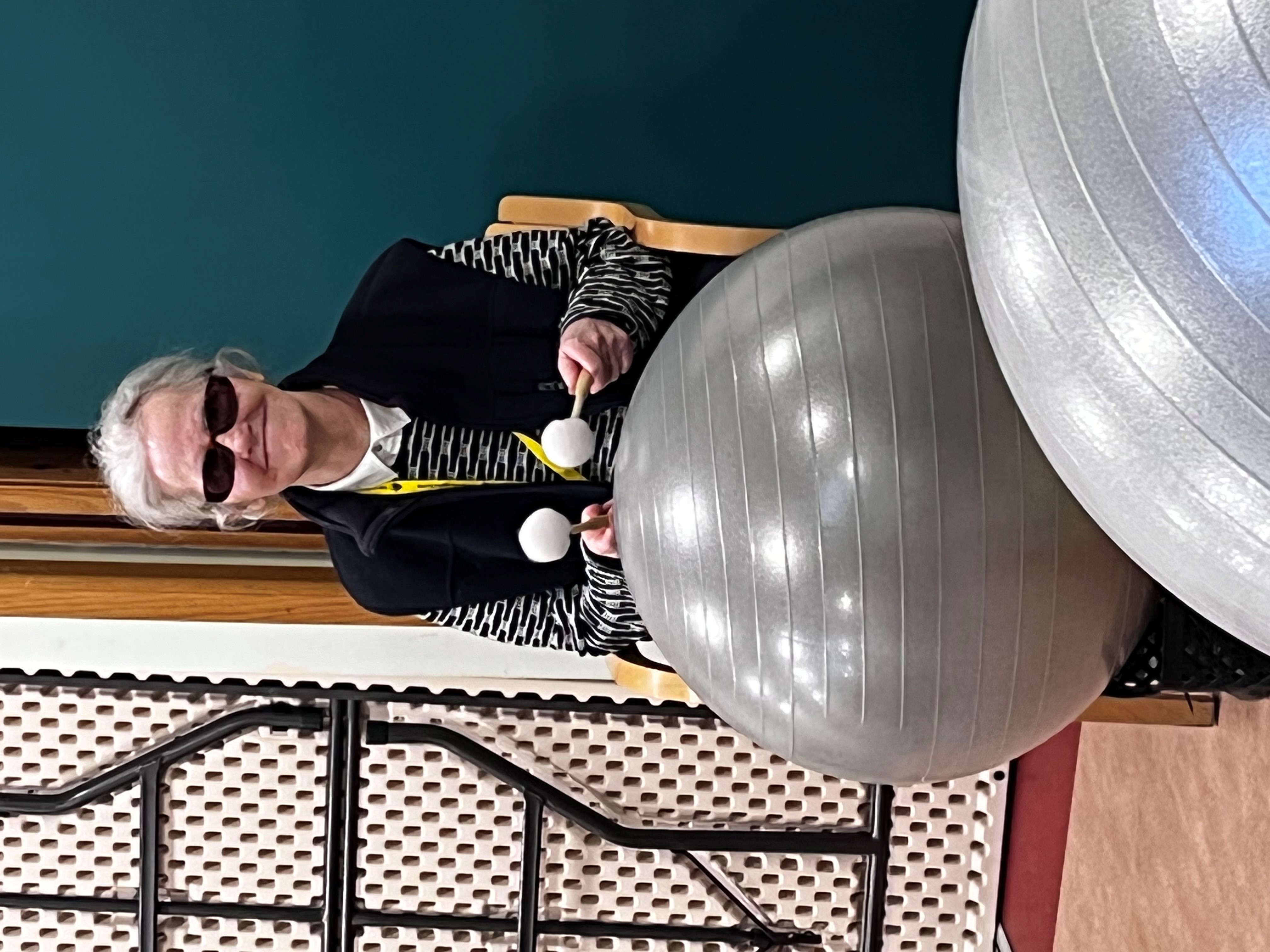 Visually impaired member smiling at the camera, sitting playing a grey fun drum.