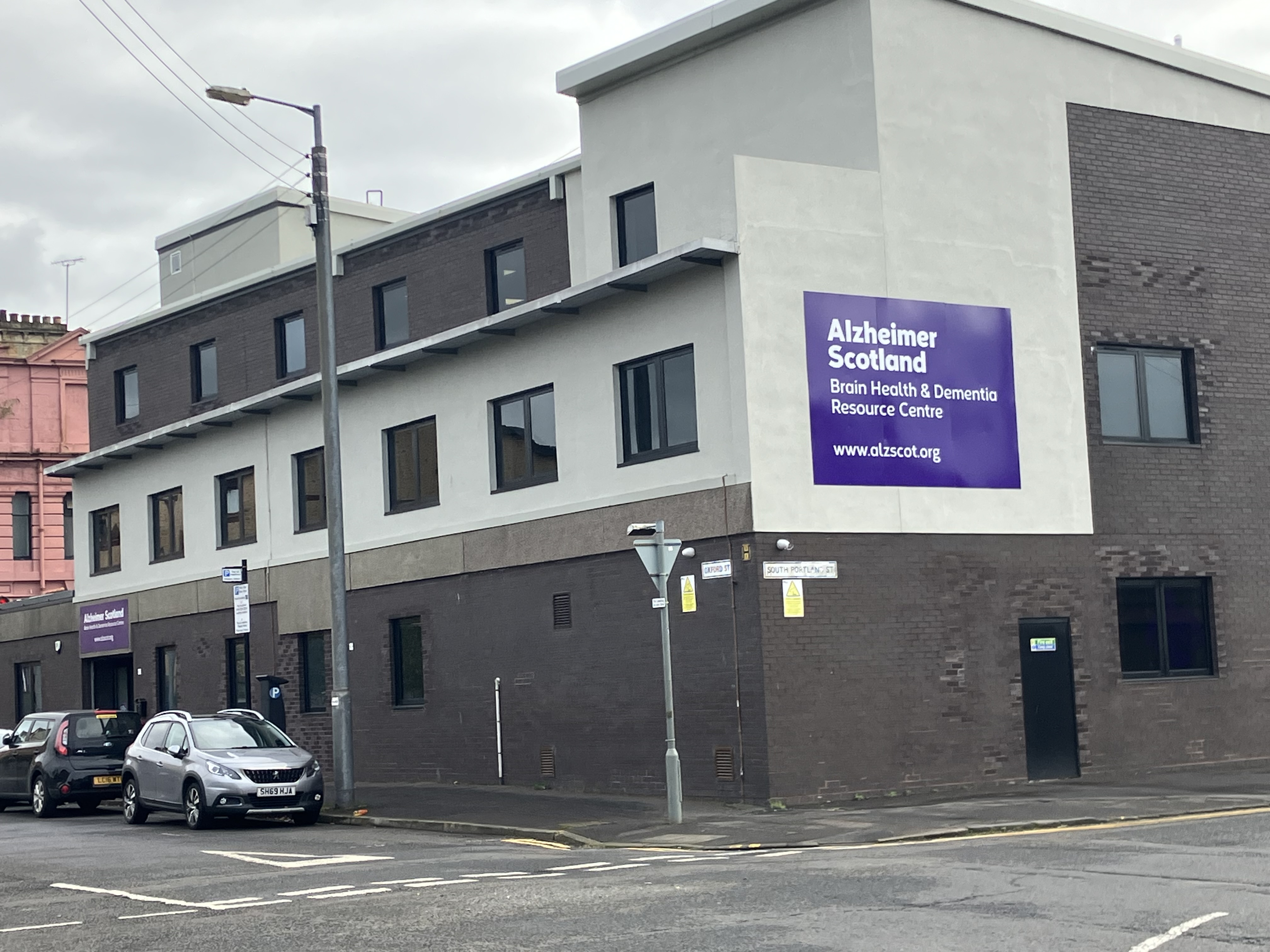 Building with a large purple sign reading "Alzheimer Scotland Brain Health & Dementia Resource Centre" with the website "www.alzscot.org." 