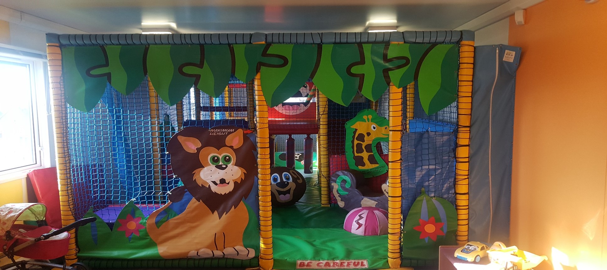 A colorful indoor jungle-themed play area with a bouncy castle and a “Be Careful” sign.