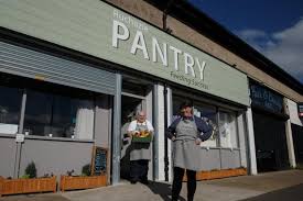 Two people standing outside Ruchazie Pantry front of shop which has a grey and white Pantry sign above the door.