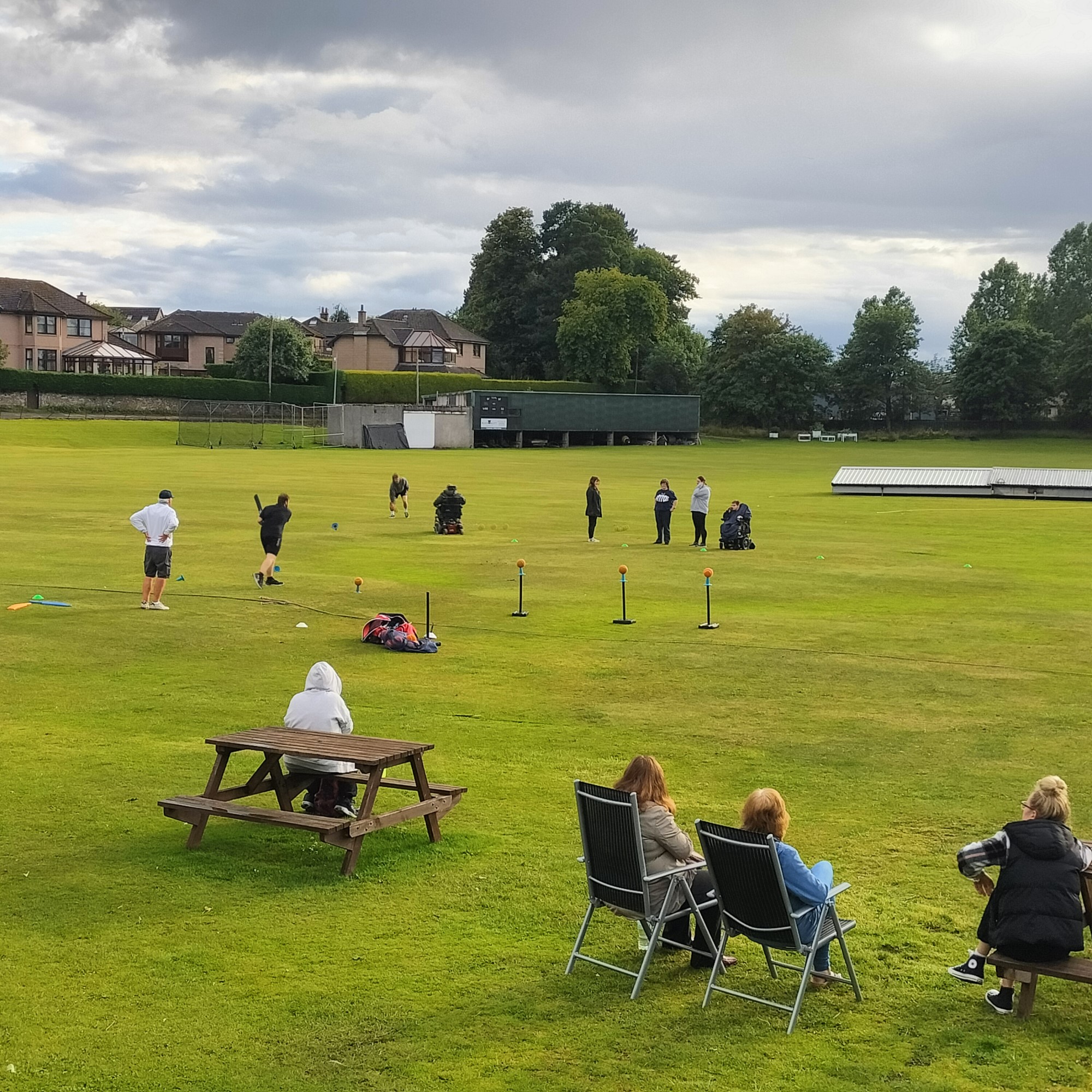Disability Cricket club members playing a game in a field with people sitting in chairs watching.